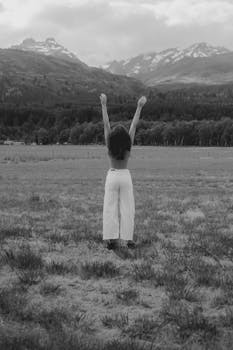 Black and white photo of a woman raising her arms towards a mountainous landscape.