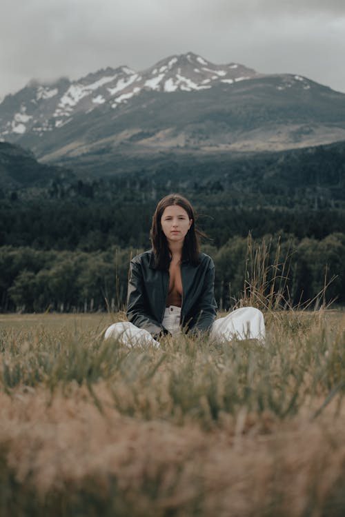 A woman sitting in the grass with mountains in the background