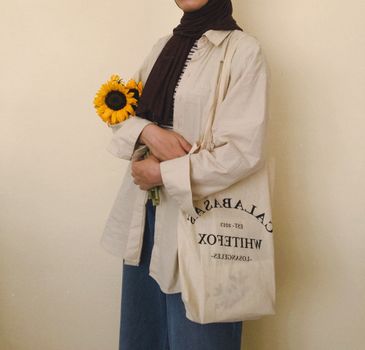 A woman in a beige outfit holds a sunflower, exuding modern and vintage fashion style.