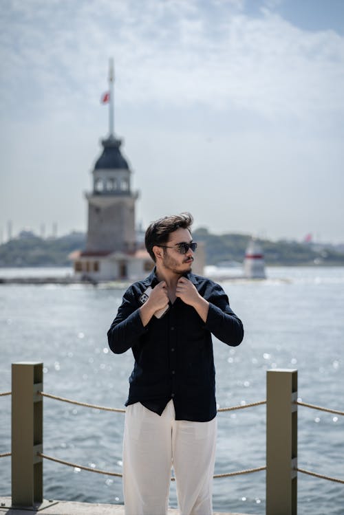 A man in a white shirt and black pants standing near the water