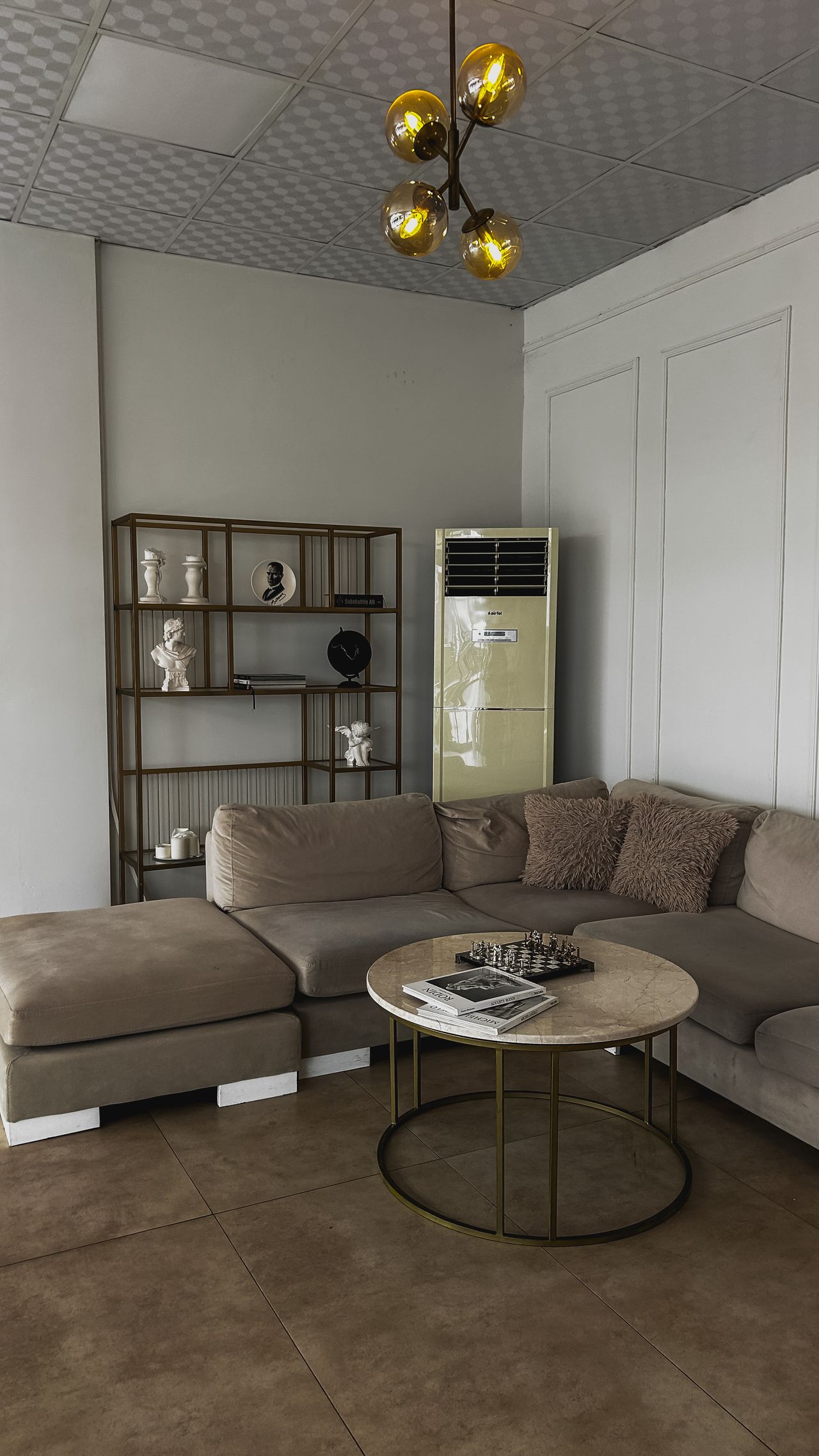 Warm taupe sectional sofa with a round marble coffee table and brass shelving
