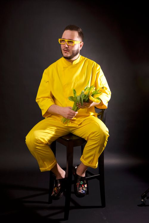 Free Stylish man in vibrant yellow outfit holding flowers, against black background. Stock Photo