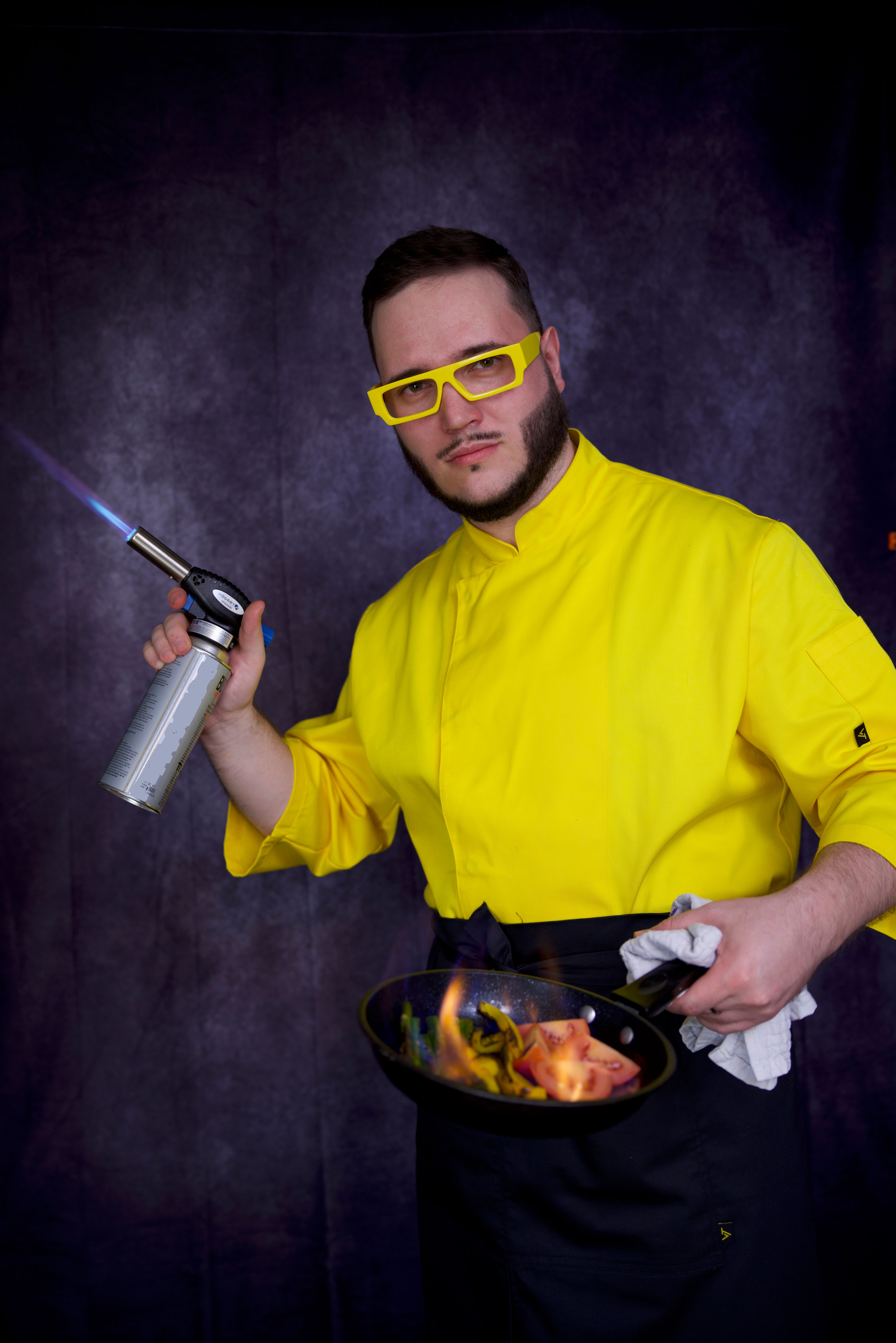Portrait of a chef in yellow attire skillfully using a blowtorch over a dish.