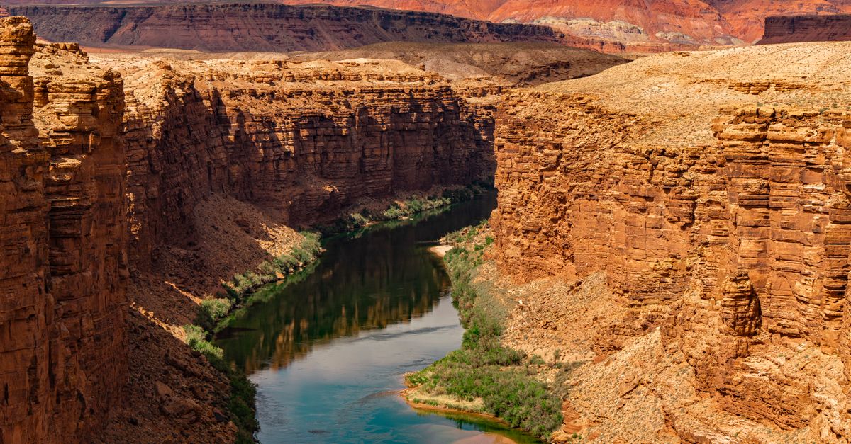 Stunning view of the Grand Canyon's rugged sandstone cliffs and serene river bend under a warm sunset.