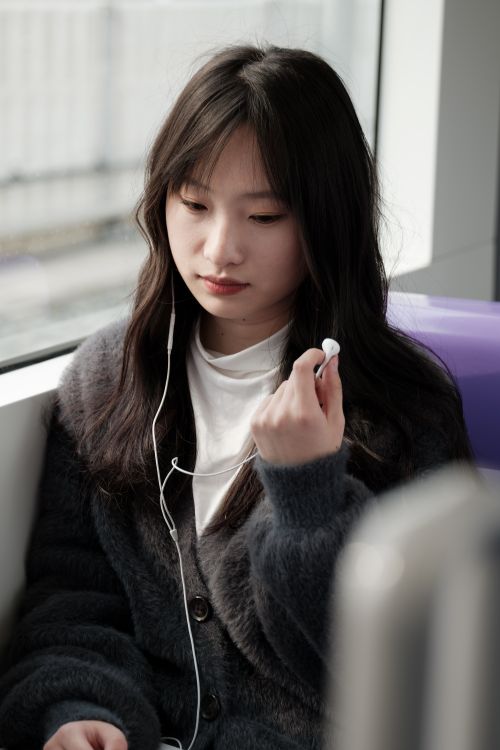 Free Asian woman with headphones on a train, enjoying her music in a peaceful setting. Stock Photo
