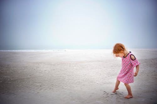 Girl playing on sand near the ocean during day time