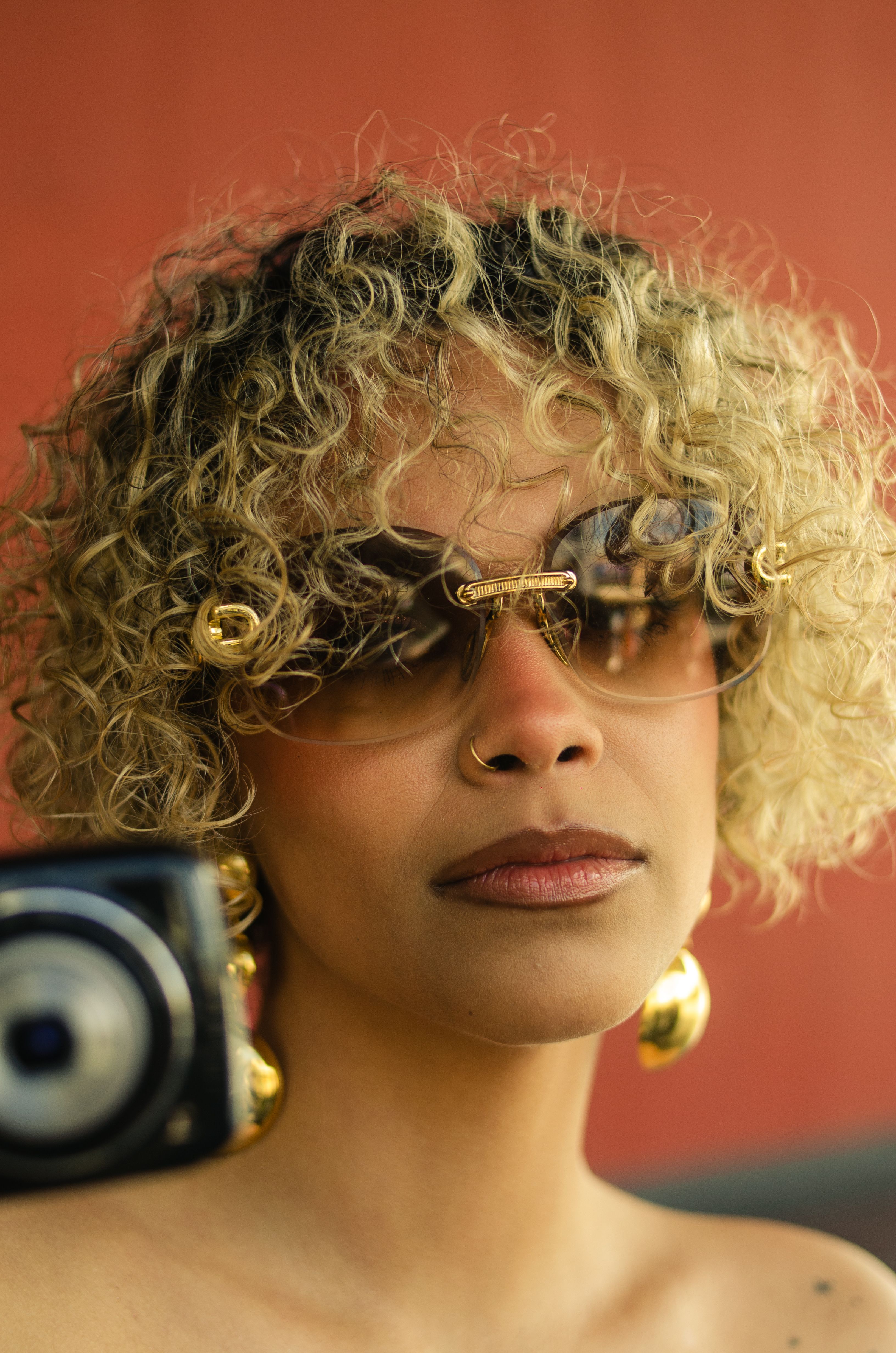 Elegant portrait of a woman with curly hair, gold earrings, and sunglasses in Bogotá, Colombia.