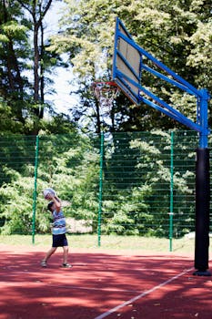 A child playing basketball on an outdoor court surrounded by trees on a sunny day.