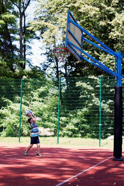 Free A child playing basketball on an outdoor court surrounded by trees on a sunny day. Stock Photo