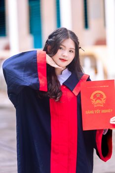 Happy graduate in gown holding diploma certificate, expressing joy and success outdoors.