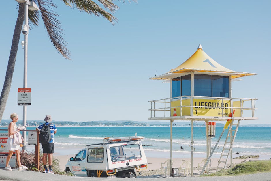 Sunny day at Coolangatta Beach with a lifeguard tower, palm tree, and people enjoying the shores.