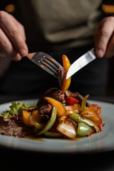Appetizing steak and vegetables served on a plate with hands using cutlery.
