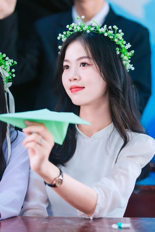 Free Portrait of an elegant woman holding a paper plane, wearing a floral wreath, with a serene expression. Stock Photo