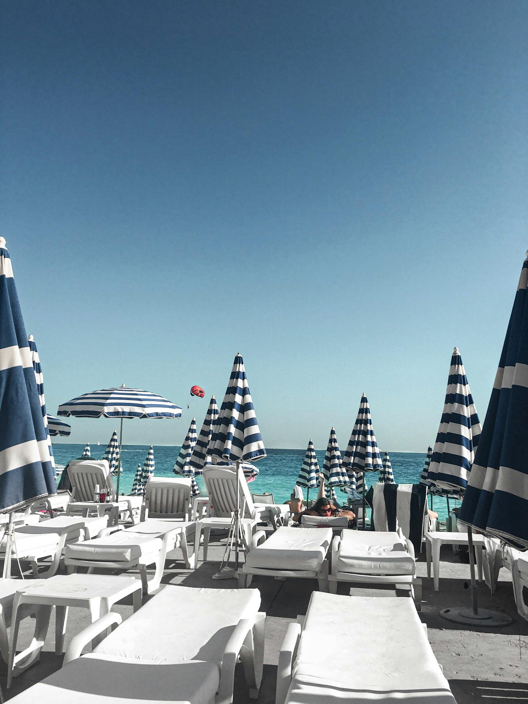 晴朗的蓝天下，热带海滩环境宜人，配有日光躺椅和条纹雨伞，令人放松