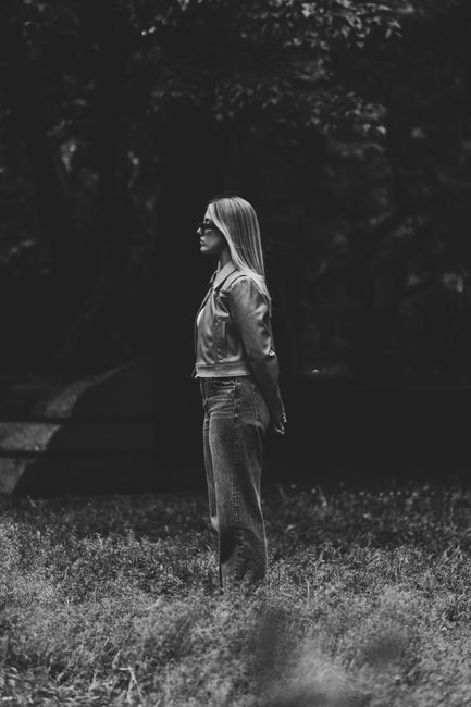 Black and white portrait of a fashionable woman standing in a park setting.