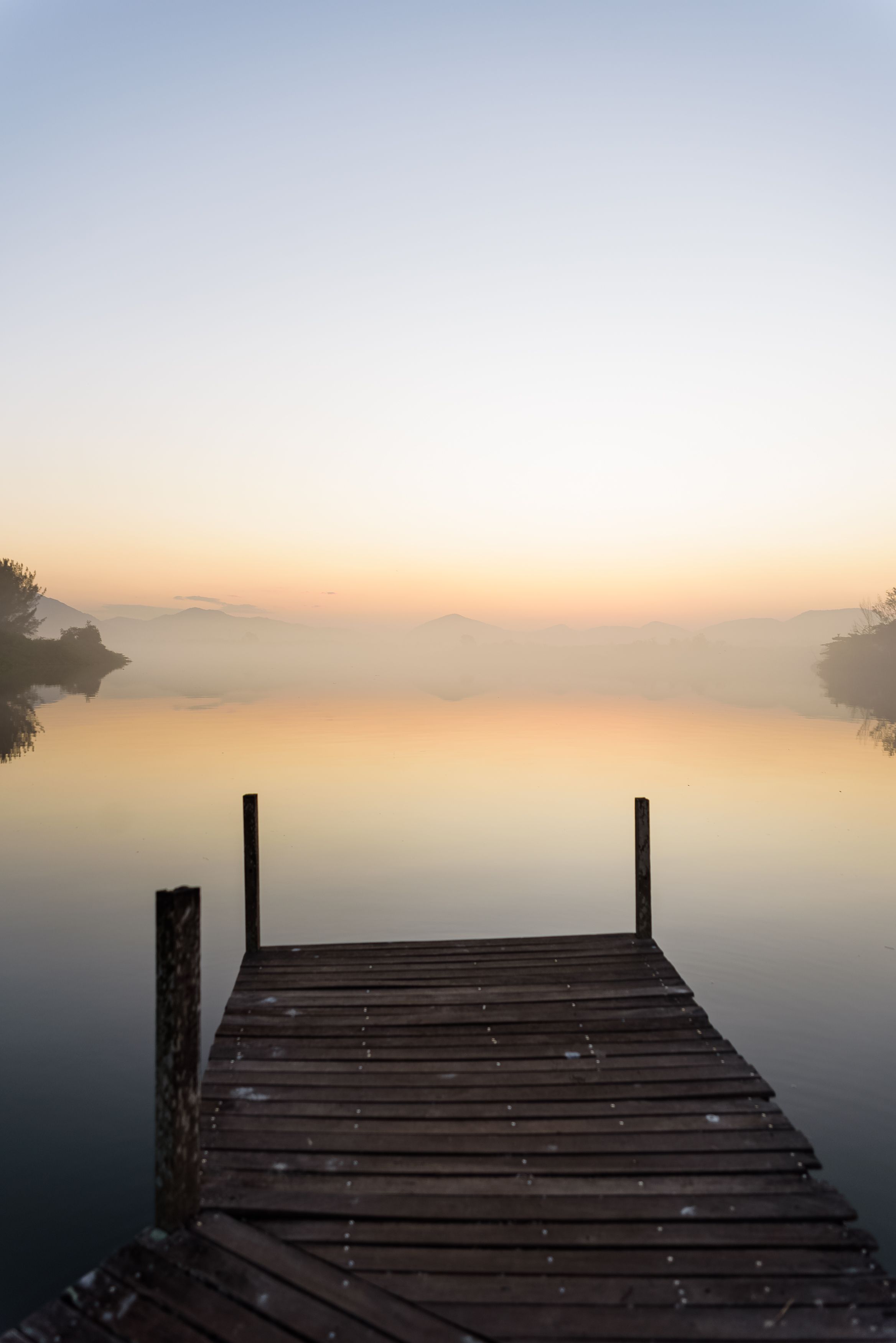 Fotomural Una escena tranquila de un embarcadero de madera que conduce a un mar cubierto de niebla al amanecer, ofreciendo una atmósfera pacífica y calmante.