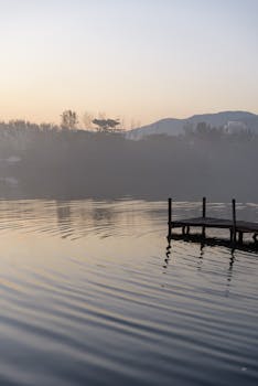 A tranquil misty lake with a wooden pier at sunrise, reflecting the calm ambiance of nature.