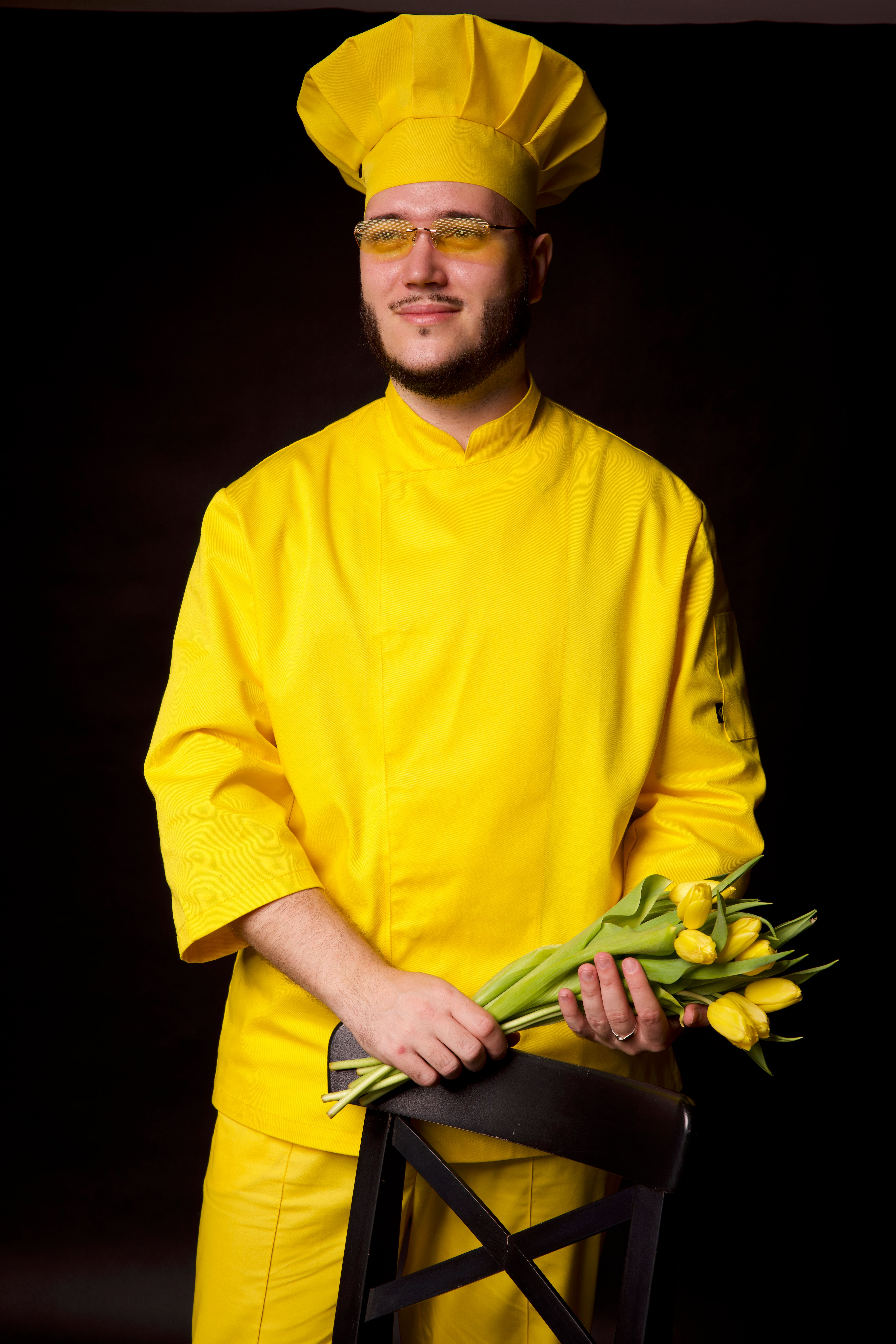 Portrait of a fashionable chef in a yellow uniform with tulips on a black background.