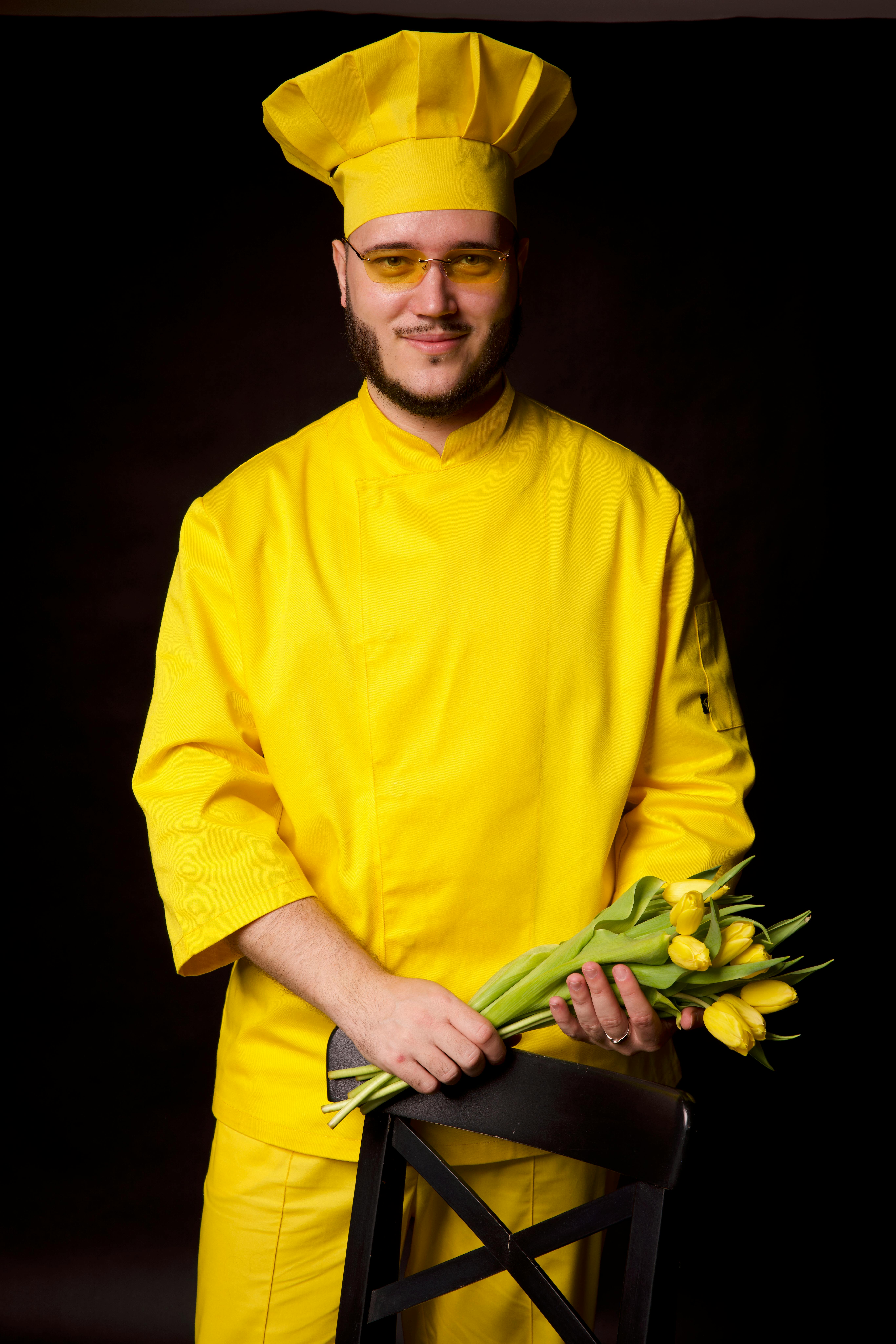 Portrait of a chef in vibrant yellow attire holding a bouquet of tulips.