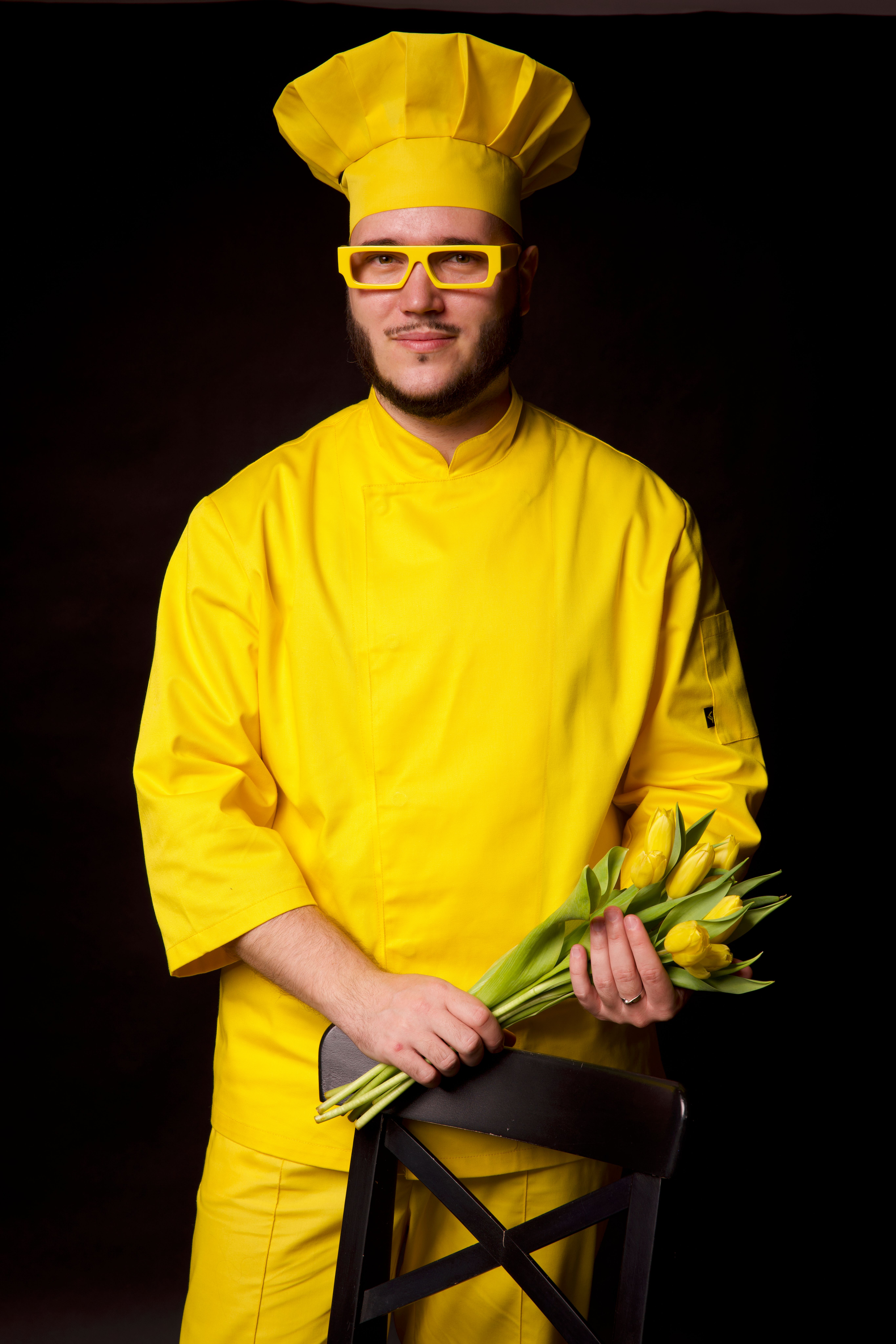 A male chef in a vivid yellow uniform and eyeglasses, holding a bouquet of tulips.