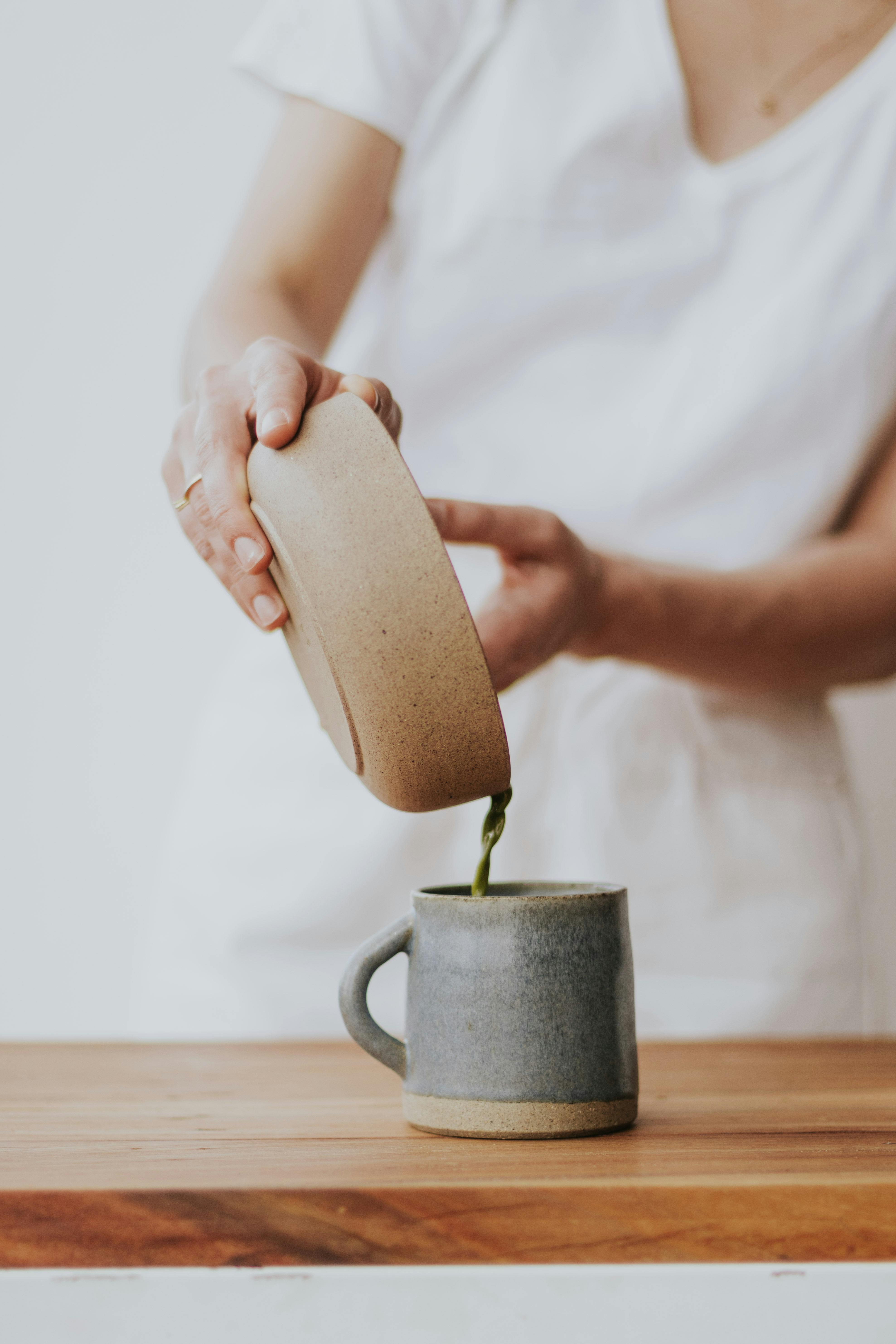 Close-up of green tea being poured into a rustic mug, showcasing natural textures.