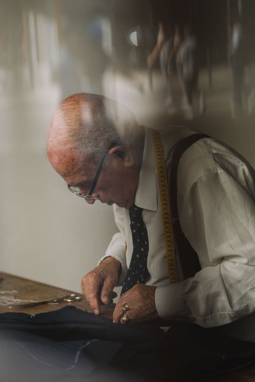 Free Senior tailor using needle and thread on fabric indoors with focus and skill. Stock Photo