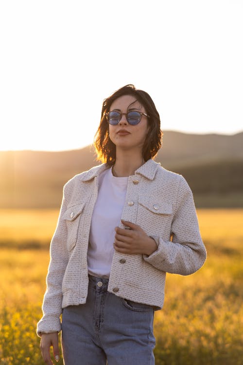 A woman in a white jacket and jeans standing in a field