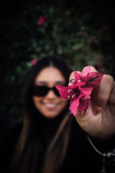 A smiling woman holds a vibrant pink bougainvillea flower, emphasizing delicate petals.
