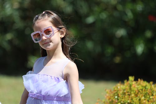 A little girl wearing sunglasses and a purple dress