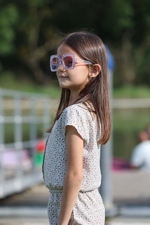 A little girl wearing sunglasses standing near a dock