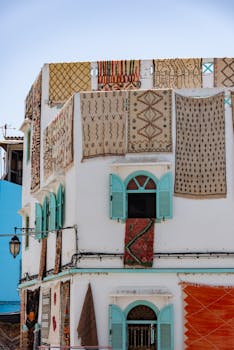 A white building in Tunis Medina adorned with colorful traditional carpets and teal shutters.