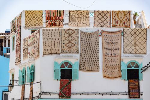 Free Traditional Moroccan rugs hanging on a white building's facade under bright daylight. Stock Photo