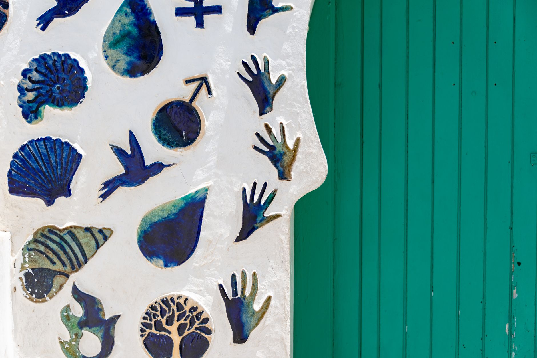 Creative wall featuring blue ceramic shapes and symbols alongside a turquoise door.