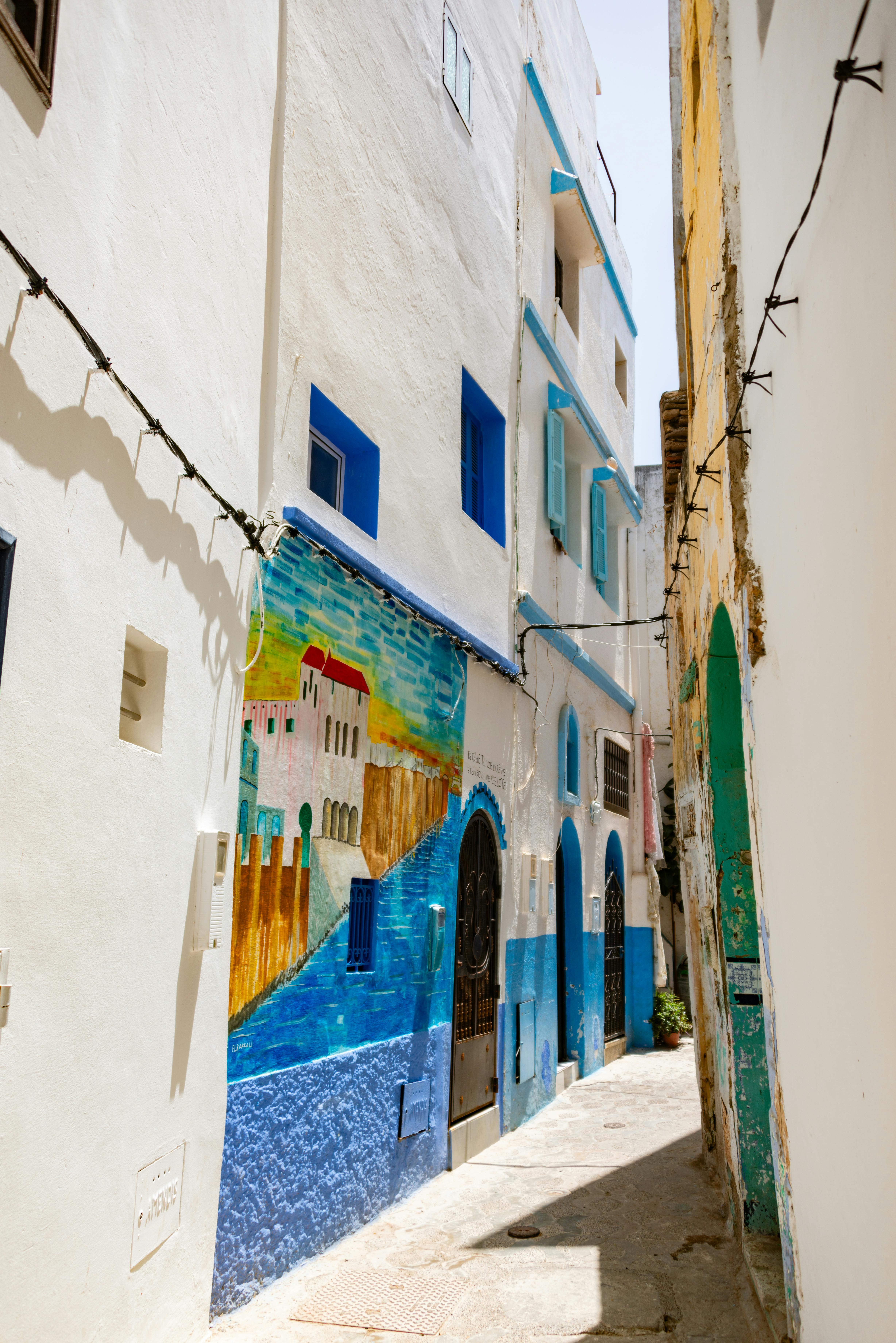 Sunlit alley with vibrant murals in a Mediterranean-style town.
