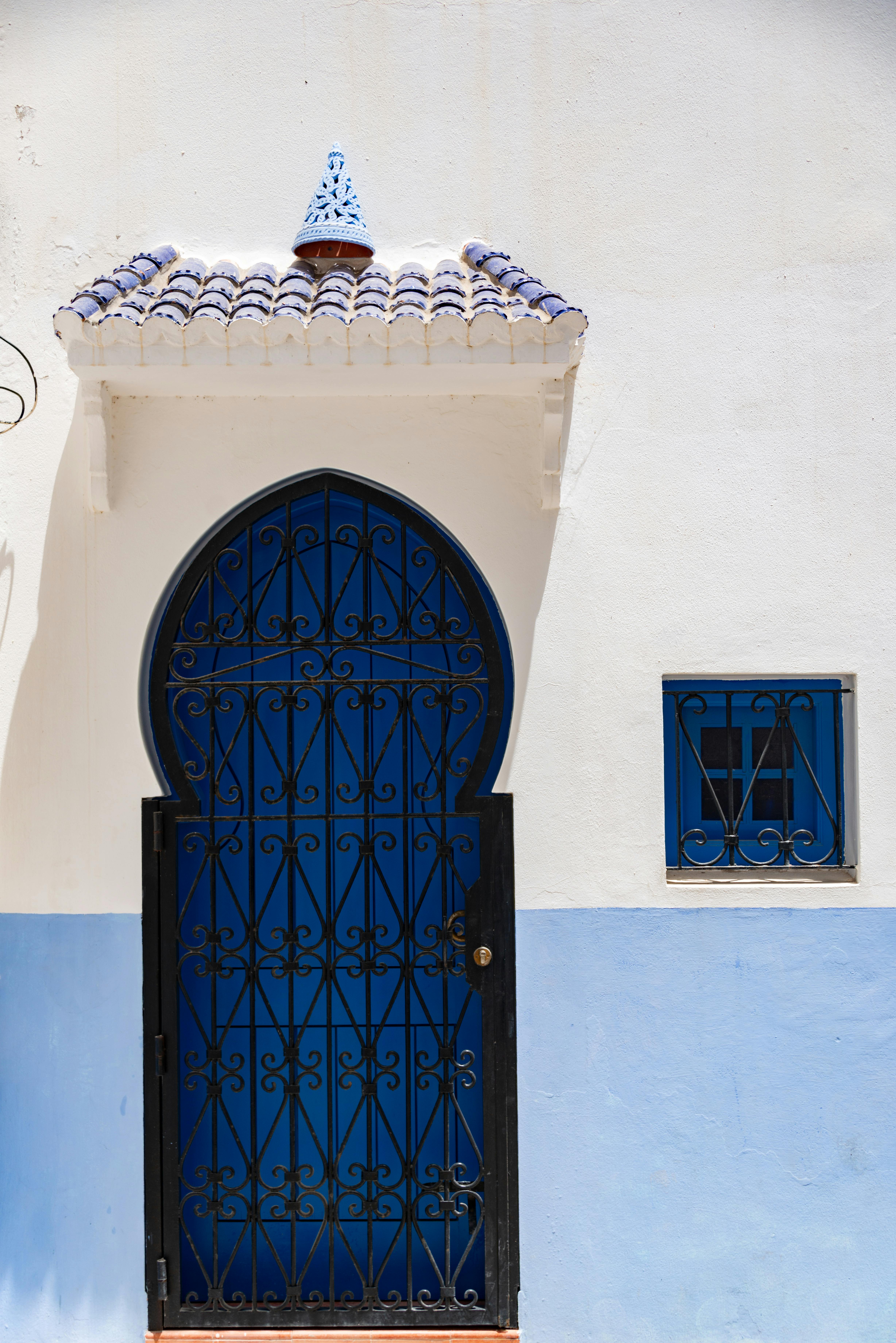 A beautiful blue arched metal door with decorative patterns in a whitewashed building facade, captured in sunlight.