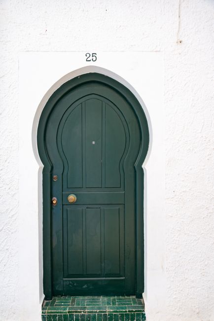 A green arched door with number 25 against a white facade.
