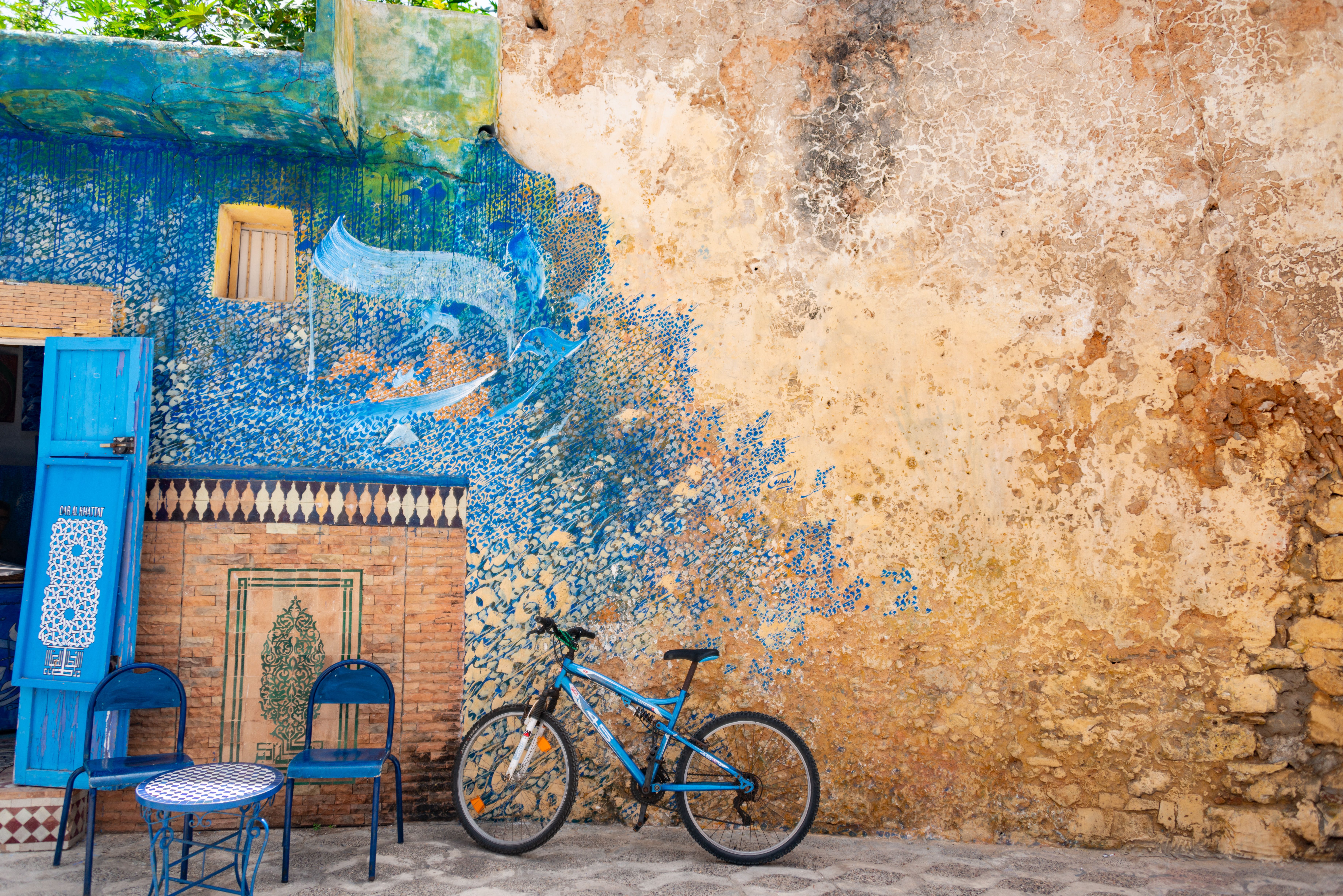 A vivid blue bicycle parked by an ornately painted wall, creating a stunning street art scene.