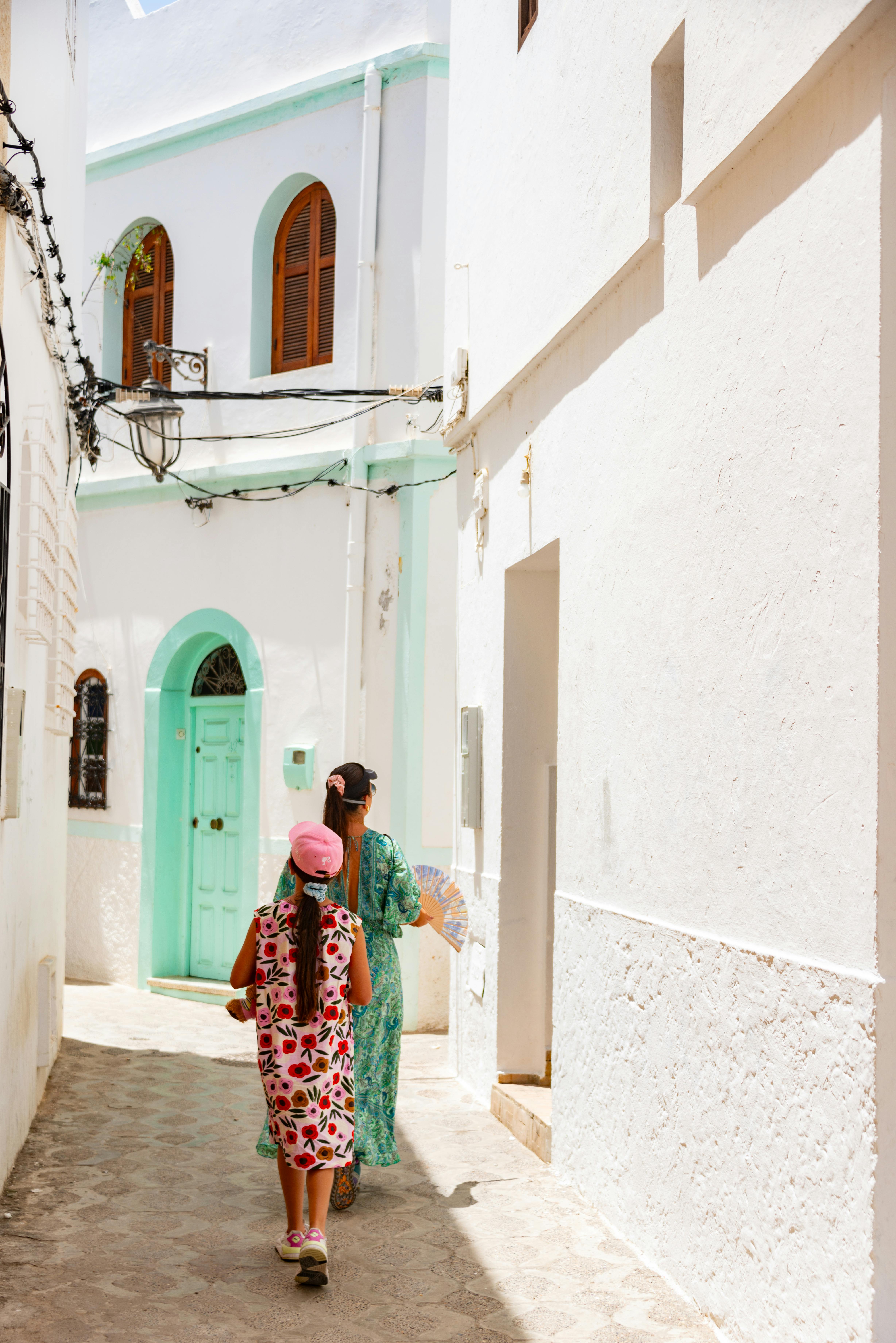 Mother and daughter walking through a sunlit white alley, enjoying a summer day.