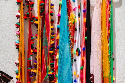 A colorful scarf hanging on a wall with many colorful pom poms