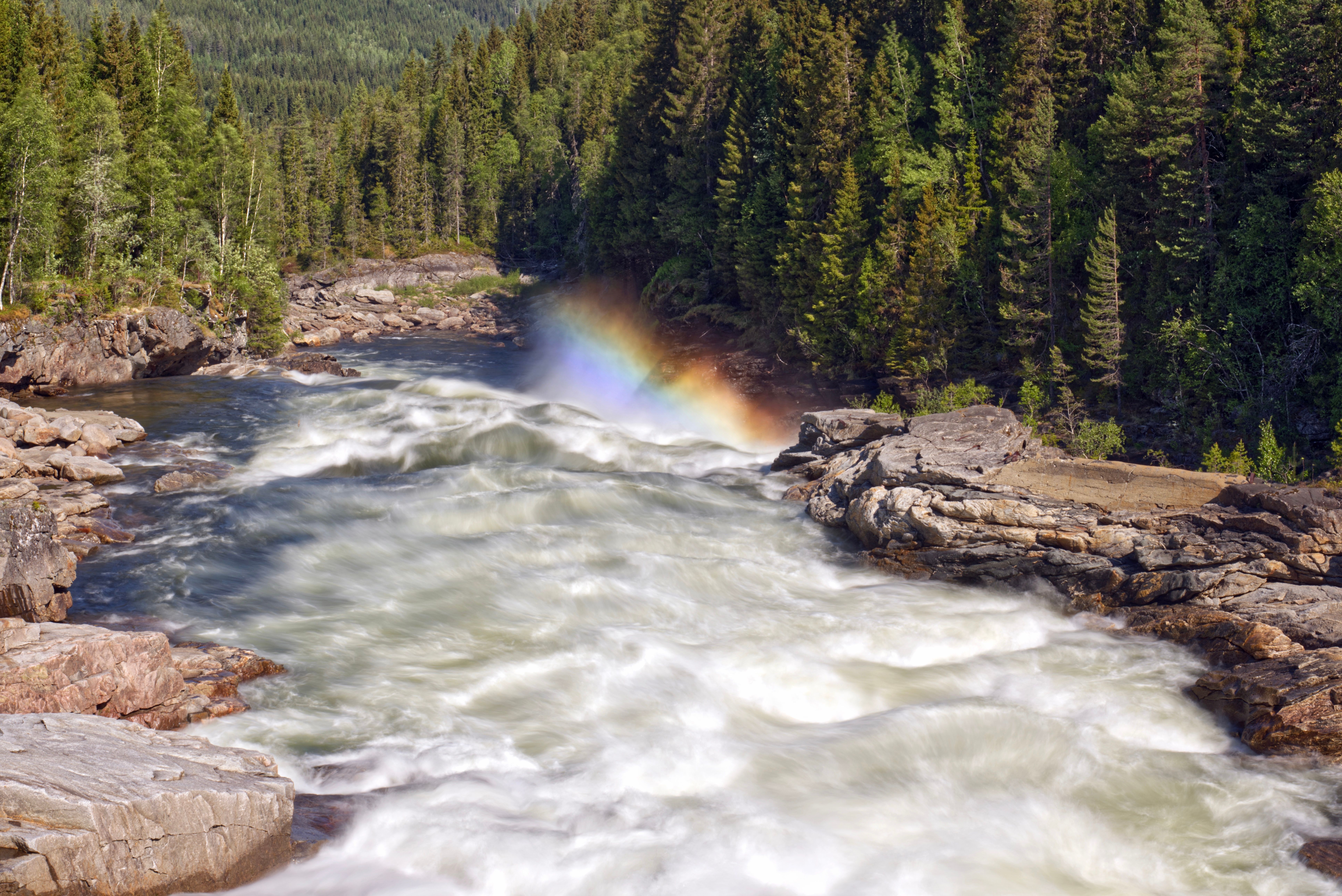 A beautiful waterfall in a lush forest with a vivid rainbow and cascading waters.