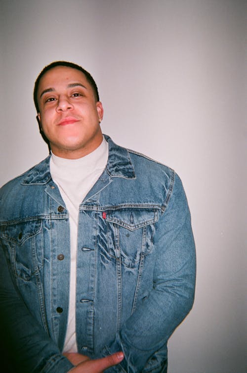 Photo of Smiling Man in White Inner Shirt and Blue Denim Jacket Posing In Front of White Background