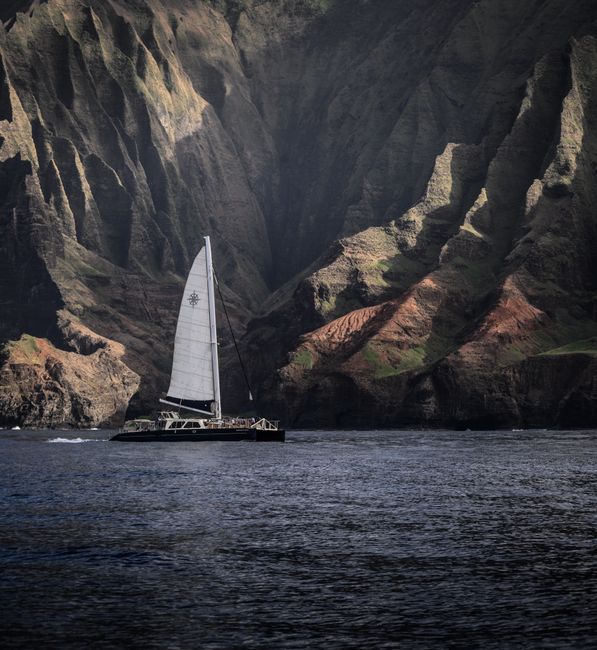 Sailboat gliding by the dramatic Na Pali Coast cliffs in Hawaii's clear waters.