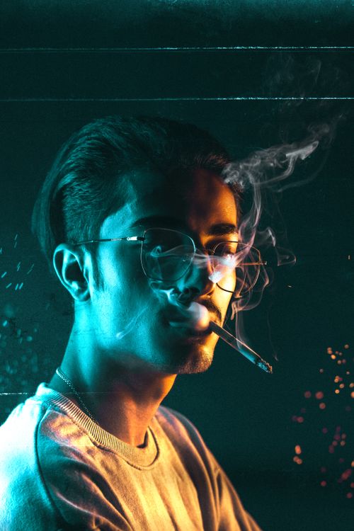 Free Dramatic portrait of a man in glasses smoking against a colorful studio background. Conceptual and artistic feel. Stock Photo