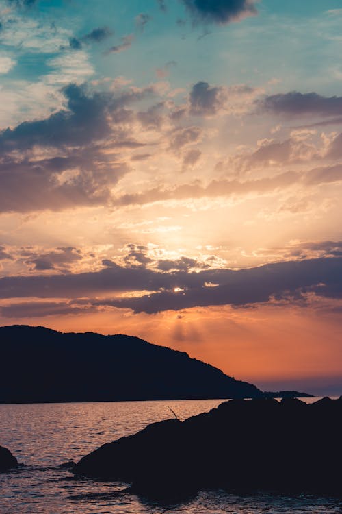 A sunset over the ocean with a rock and a person