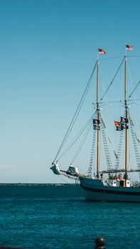 Tall sailing ship adorned with flags against a clear blue sky on a calm sea.