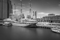 这张黑白照片拍摄了一艘停泊在曼哈顿海滨的帆船，展现了标志性建筑与宁静的港湾景观