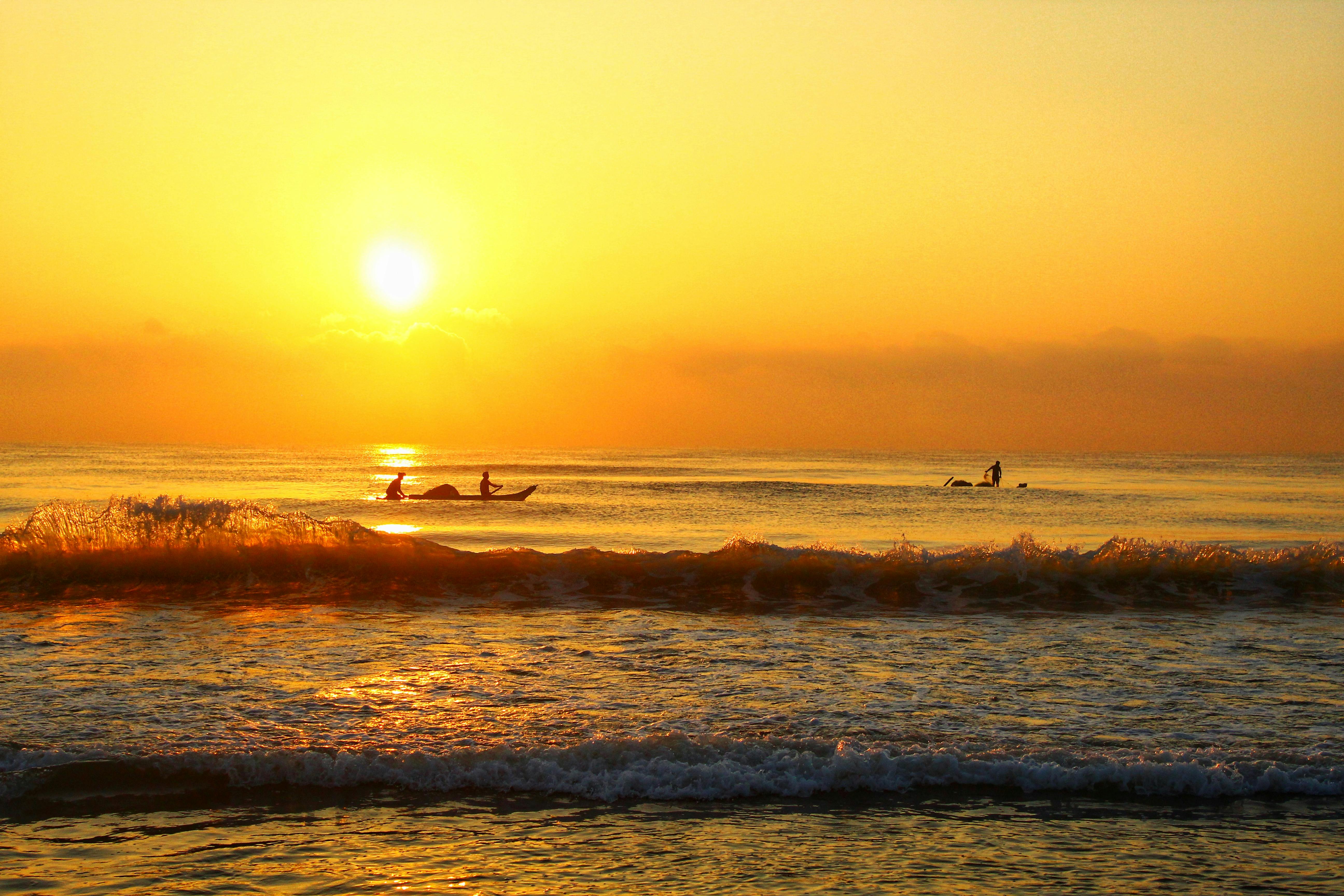 日出时分，渔民在宁静的海面上劳作，头顶是充满活力的橙色天空