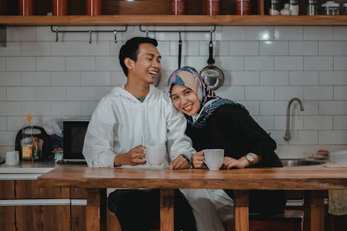 Women Wearing Hijab Leaning on a Man Near a Brown Table