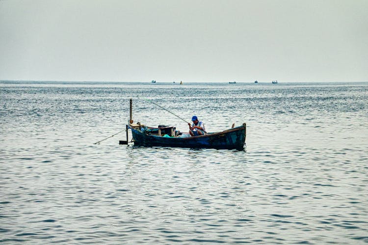 Man Sitting On Fishing Boat On Calm Body Of Water