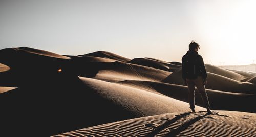 Free A solitary figure stands on sand dunes at sunset in a vast desert landscape. Stock Photo